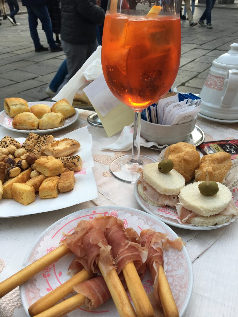 Enjoying aperitivo hour, and every hour in Monza. Image shows an Aperol spritz and a spread of snacks outside a bar in Monza