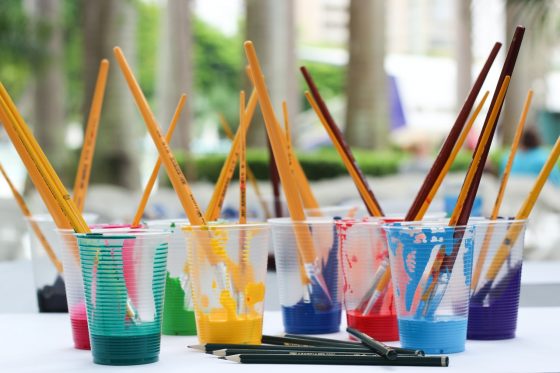 image shows different plastic cups of paint with brushes in them
