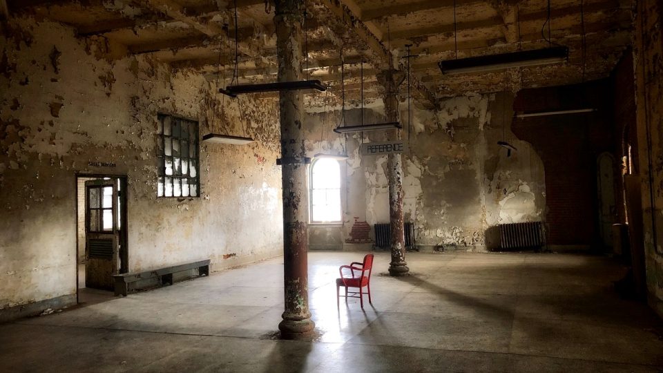 Image shows inside an old empty building with one red chair in the middle