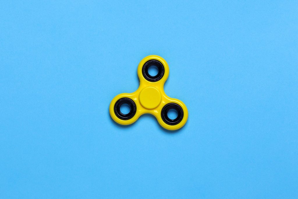 Image shows a yellow fidget spinner on a blue background