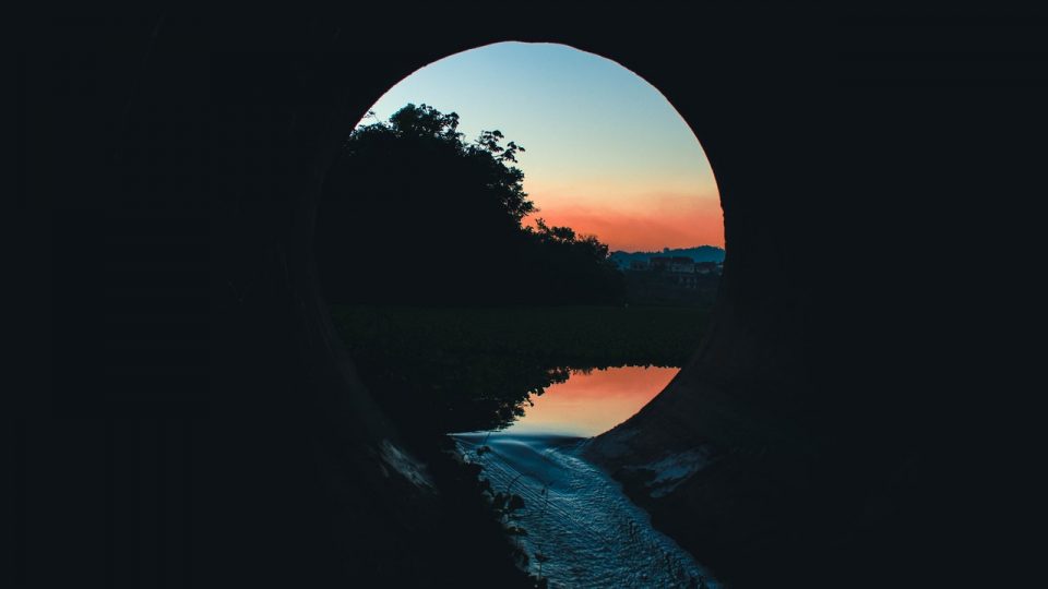 Image shows a sunrise at the end of a tunnel, reflected in water