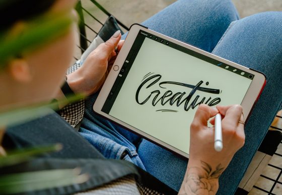 Image shows person working on a tablet with the word "creative" in a calligrapy type scrip