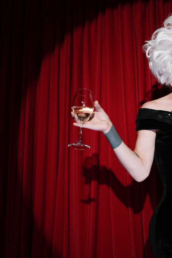 Red velvet curtain with a spotlight falling on a woman's arm holding a glass of wine. 