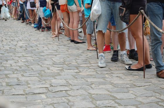 Image shows a long line of people queueing for something with just their legs and feet visible