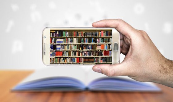 Image shows an image of a library of books on a smartphone screen with a real book on a table in the background How do you collect stories about what you do.