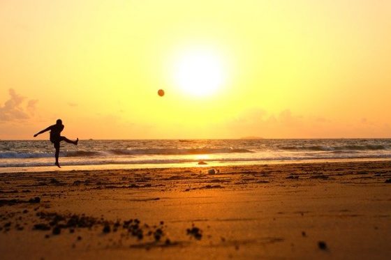 Image shows a person kicking a football on a beach at sunrise or sunset. What to write about when you don't do football.
