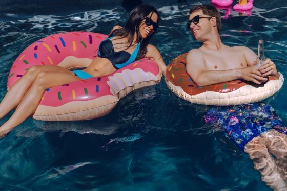 Image shows a man and a woman in a swimming pool in inflatable doughnut rings.