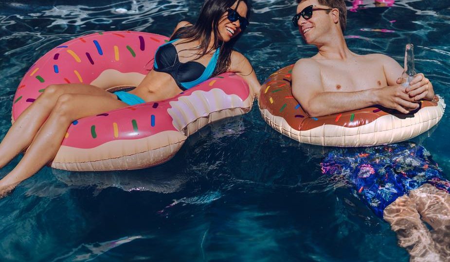 Image shows a man and a woman in a swimming pool in inflatable doughnut rings.