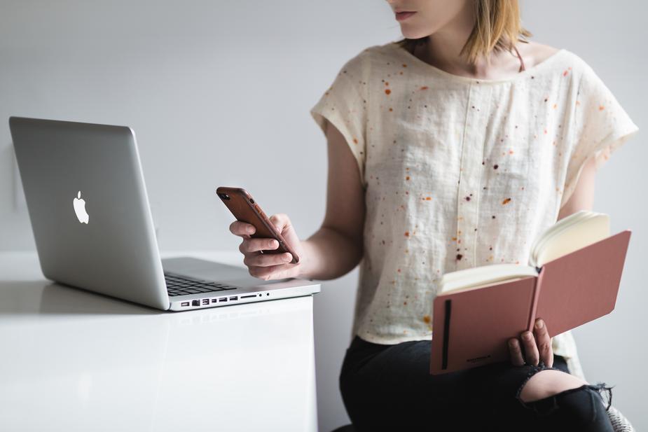 Image shows a woman with a book open, staring at a phone screen and a laptop screen. The art of not thinking and the cult of busy.