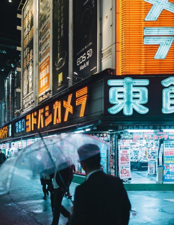 Commuters on a neon lit Tokyo street. How to go anywhere when you can't go anywhere.