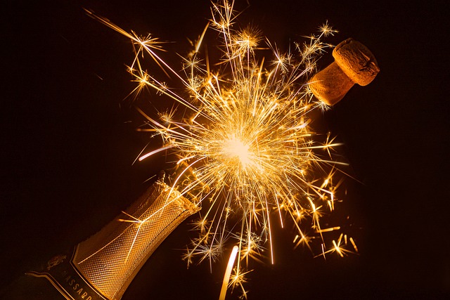 Image shows a champagne bottle with a popping cork and a lit sparkler