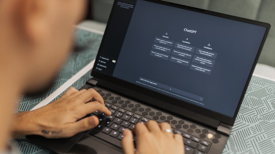 Image shows someone working on a black laptop with the homescreen of ChatGPT open on the screen